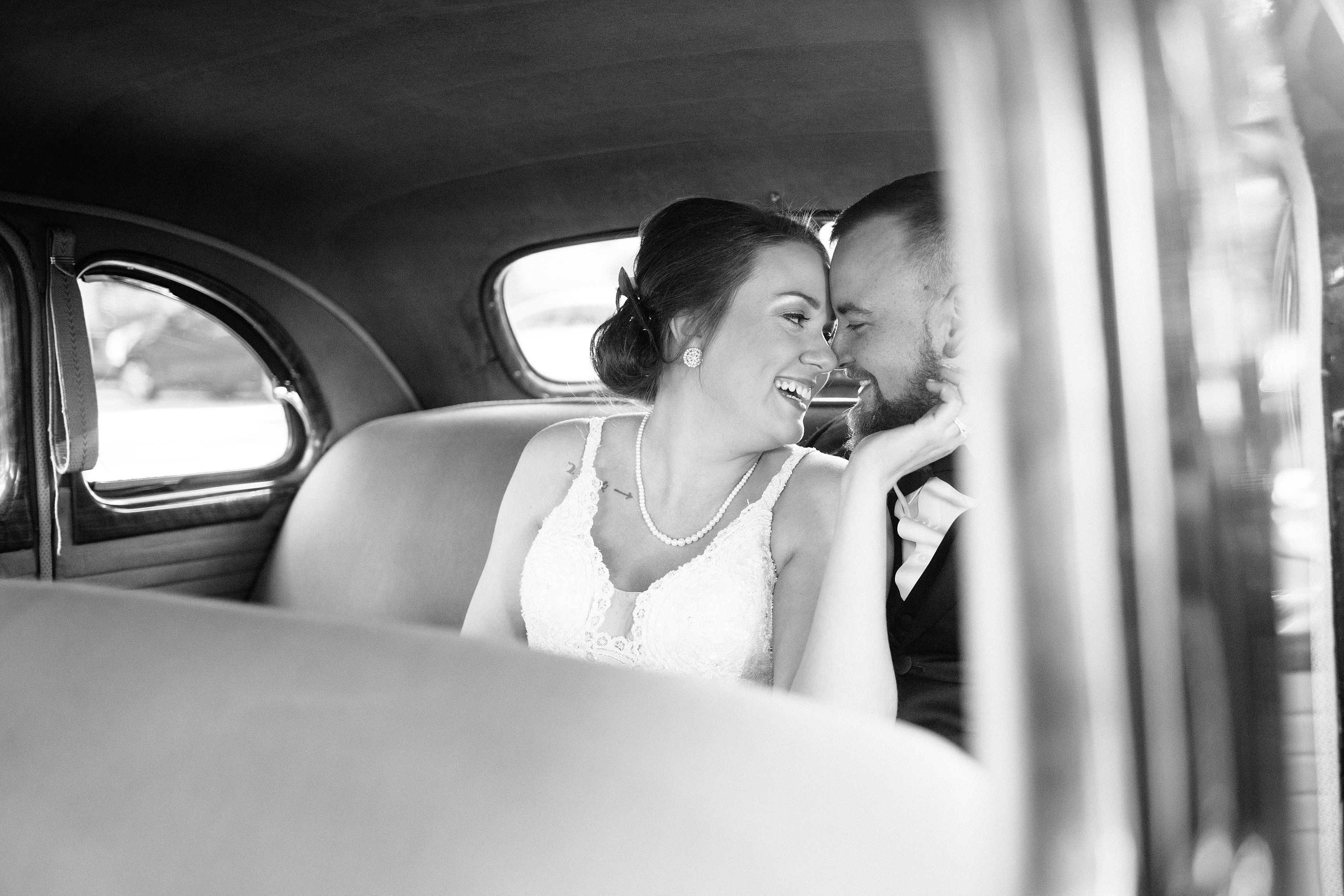 Black and white photo of bride and groom in old car.